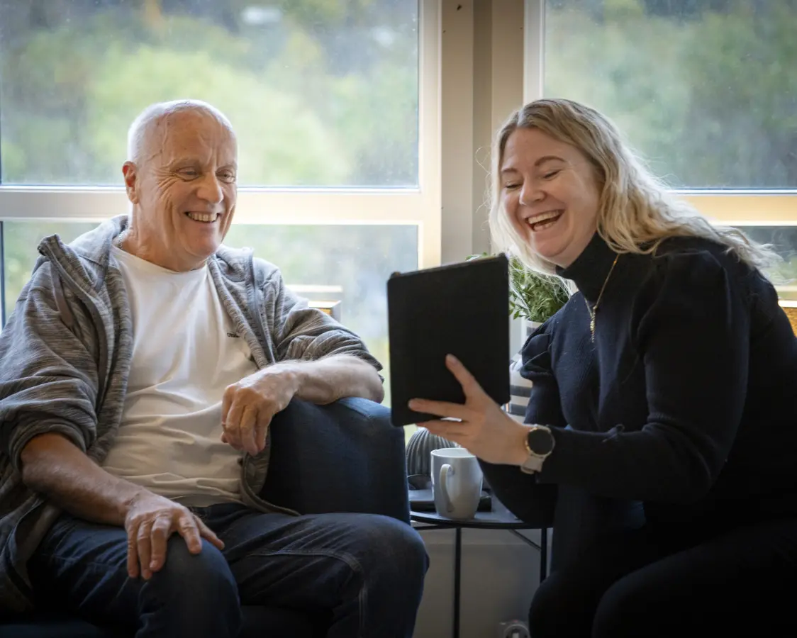En eldre mann og ung kvinne sitter og ser på en ipad