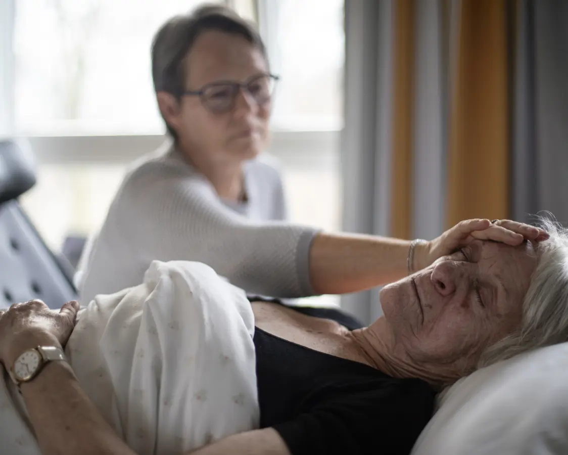 En kvinne sitter ved sykesengen til en eldre kvinne