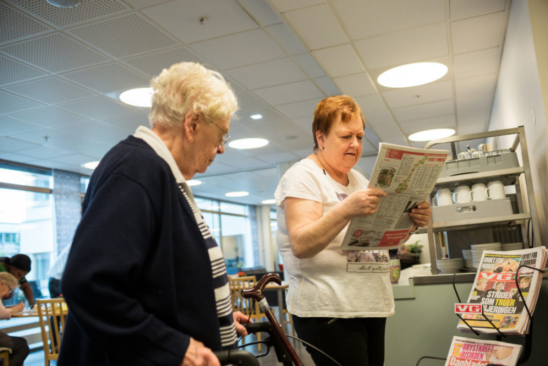 En kvinne leser papiravis og en annen kvinne ser på.