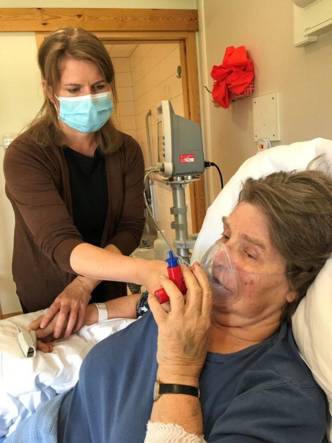 Kvinne med munnbind hjelper kvinne med pustemaske. TO UKER ETTER: Det har gått to uker siden hjerneblødningen, og Jorunn trenger fortsatt hjelp til det meste. Her får Jorunn hjelp av sin datter med PEP-masken. Foto: Privat