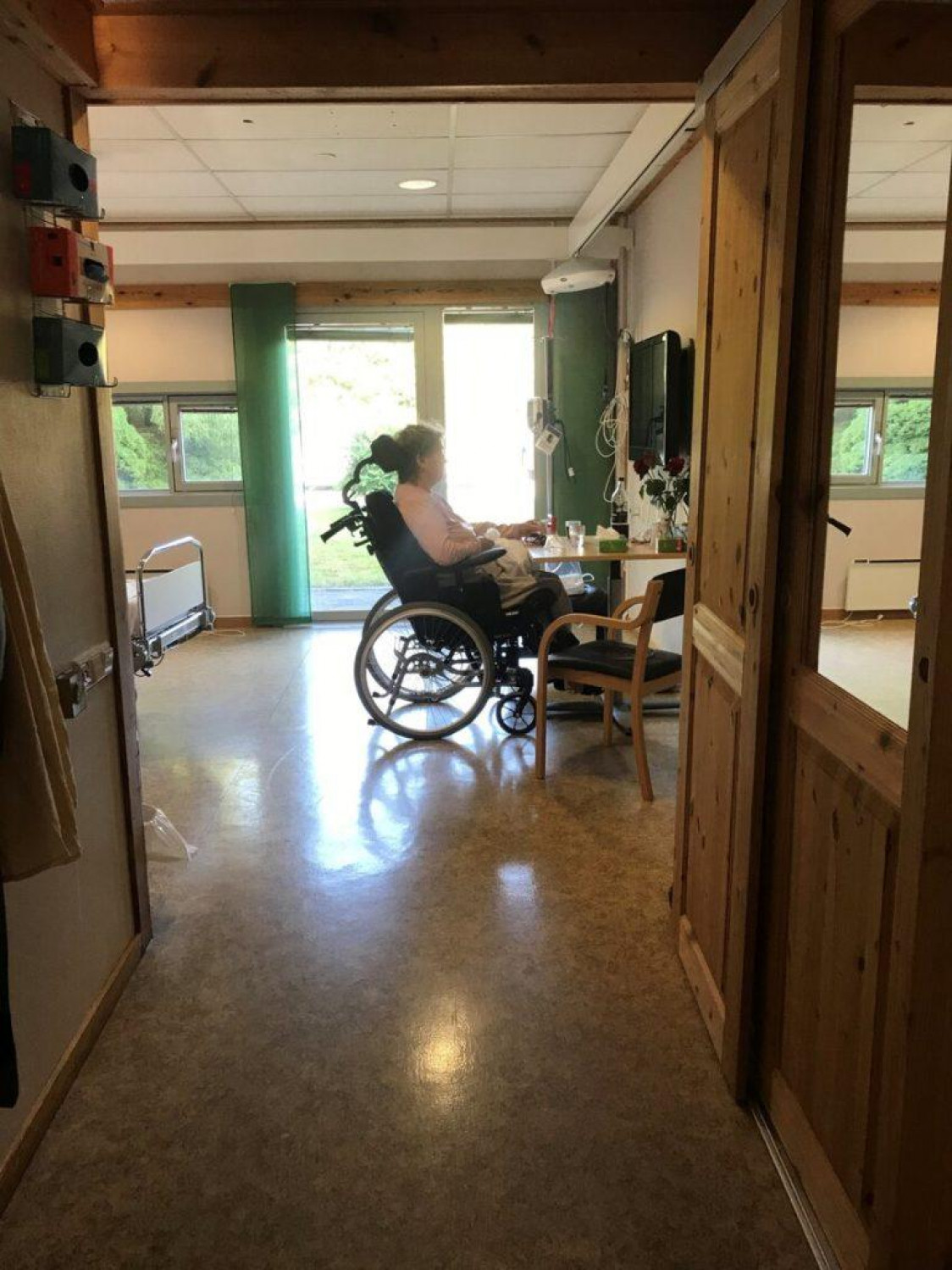 Kvinne i rullestol inne på et pasientrom. SENSOMMEREN: På sensommeren er Jorunn på rehabilitering. Hun klarer ikke å gå og må sitte i rullestol.