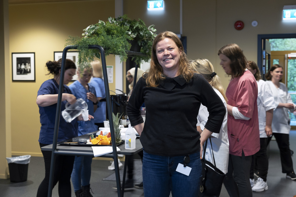 Kvinne foran med mange personer bak i rommet.