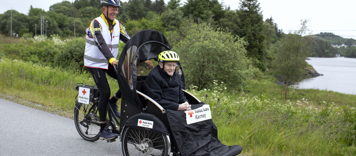 Frivillig sykler en rickshaw med eldre mann som passasjer