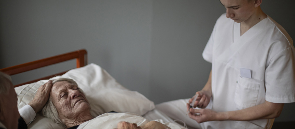 eldre dame ligger i sengen og skal dø med sykepleier ved siden