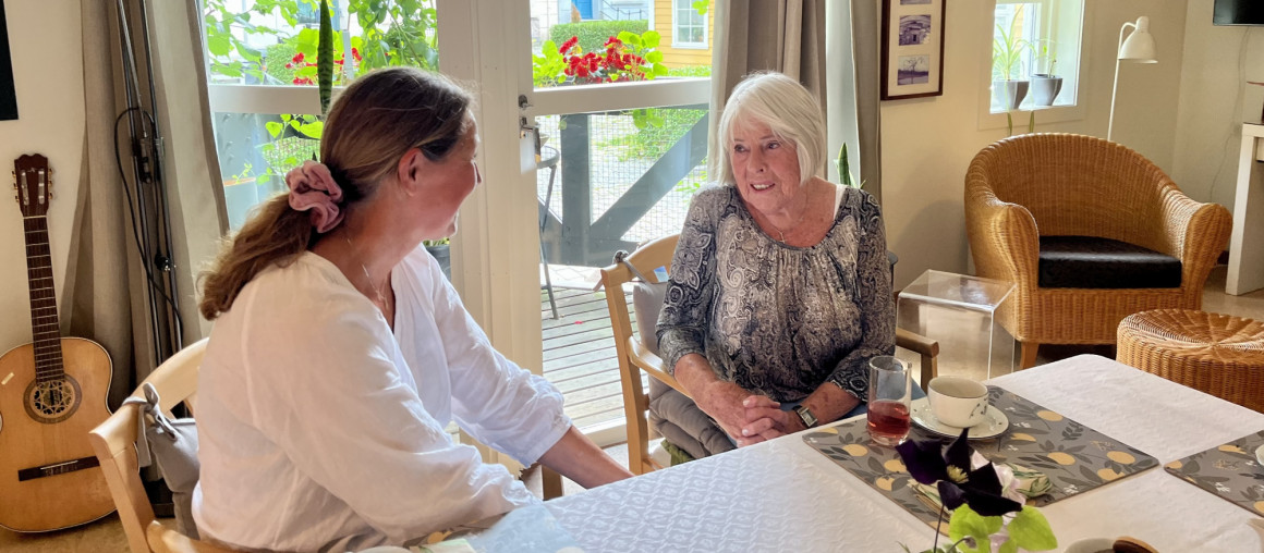 eldre dame sitter i samtale med yngre dame i en stue