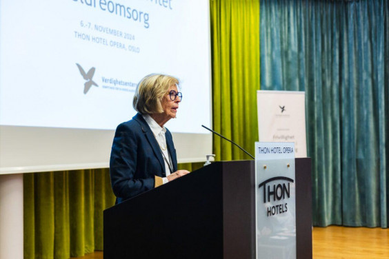 en voksen dame står på talerstolen på en konferanse om frivillighet