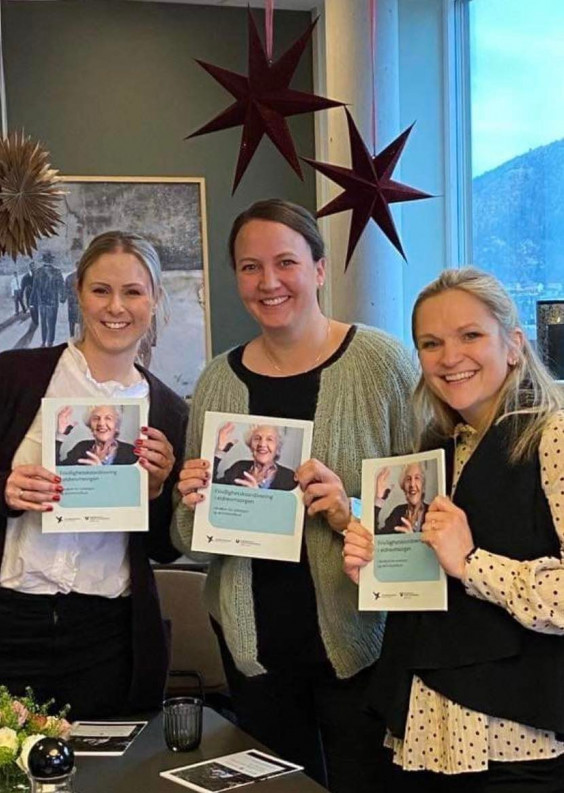 Tre smilende kvinner holder en bok