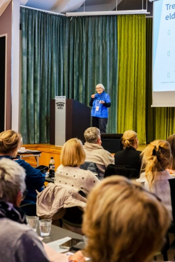 en eldre dame prater til en stor forsamling